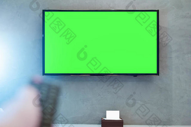 带绿色屏幕合成的LED屏幕电视。电视或电视-现代房间墙壁上的绿色屏幕，遥控器上的手模糊