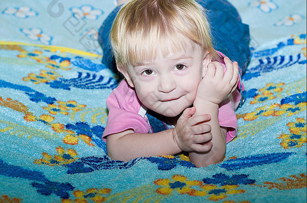 婴儿躺在床上，身上衬着鲜艳的蓝色格子花黄色花朵，她微笑着