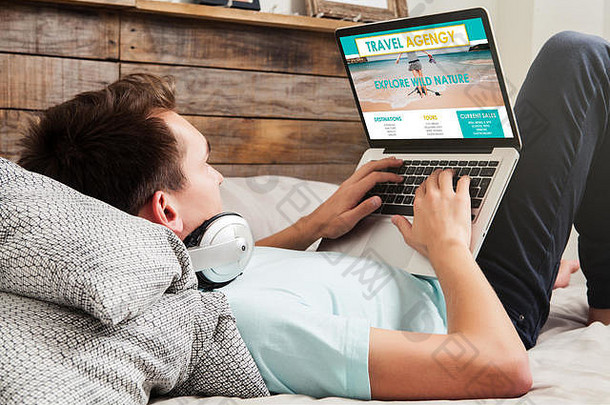 一名男子躺在家里的床上，用笔记本电脑在互联网上搜索旅游目的地。