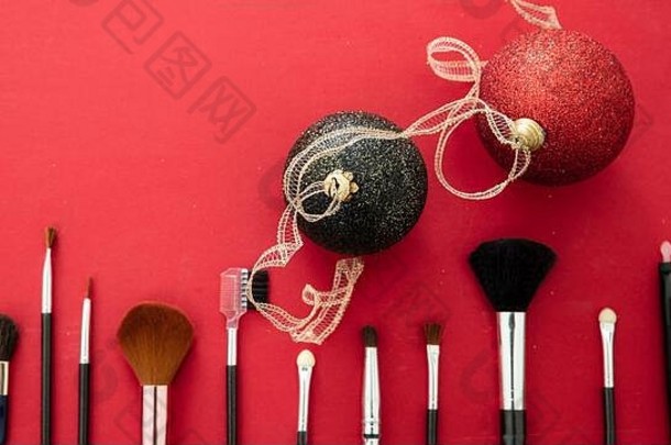 化妆圣诞派对概念。在红色背景、俯视图上设置化妆刷和圣诞球。专业化妆工具