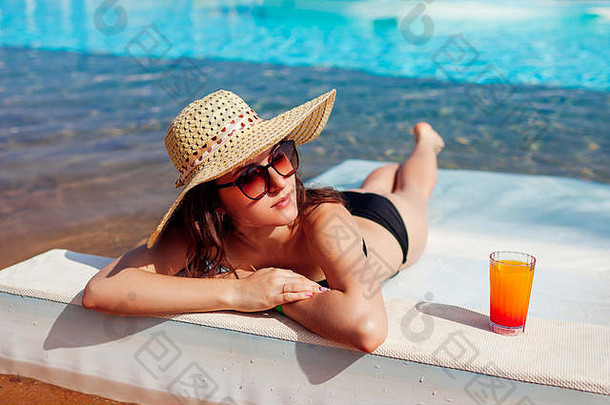 穿着比基尼的女人躺在躺椅上，在酒店游泳池里放松，喝着鸡尾酒。暑假一价全包