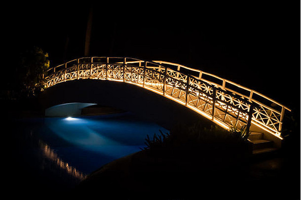 夜间游泳池上方照明的人行桥的长时间曝光。