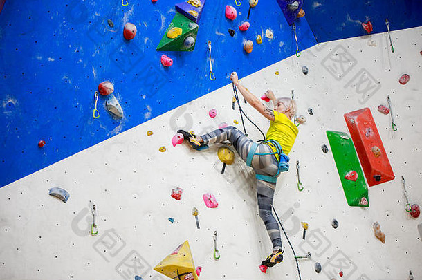 图为身穿黄色T恤的年轻女运动员在训练中爬上<strong>墙</strong>壁的照片