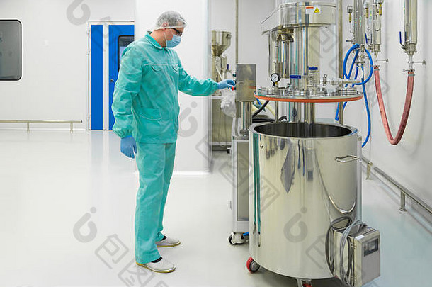 制药厂工人穿着防护服，在无菌工作条件下与控制面板一起工作