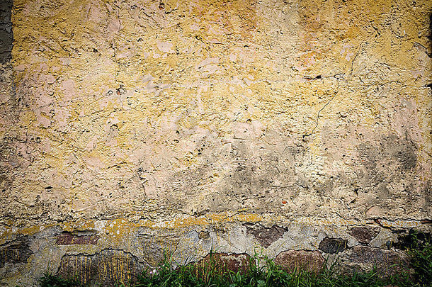 旧的开裂的黄墙和一些草