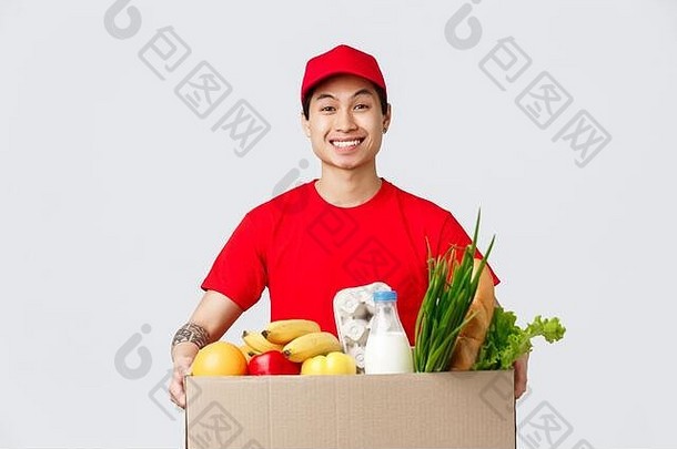 网上购物、食品配送和网店概念。一个戴着红帽子、身穿t恤、面带笑容的亚洲小伙子，手里拿着一个装满新鲜食品的盒子
