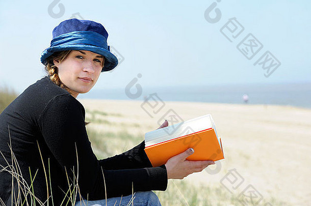 年轻的女人蓝色的他阅读书海滩