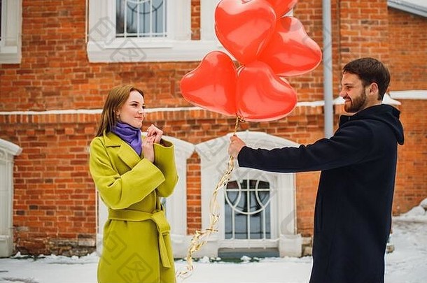 一对可爱的白种人情侣在浪漫约会。男人送给美丽的女士红色的气球作为礼物。有爱心的男人给女人安排了一个假期。红砖b
