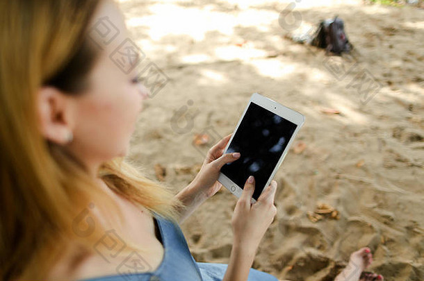在沙子背景下使用平板电脑的年轻女子。