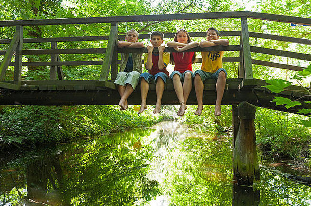 四个孩子坐在一座木桥上，双腿悬空。