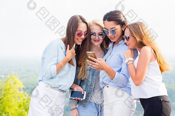 使用智能手机、互联网、应用程序和信息。一群漂亮的女孩看着电话里的女朋友笑了起来，惊讶不已
