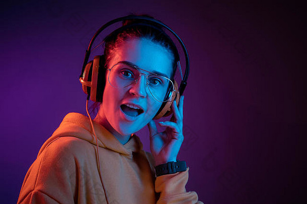 在演播室里，戴着耳机在红色霓虹灯背景下听音乐的时尚美女。