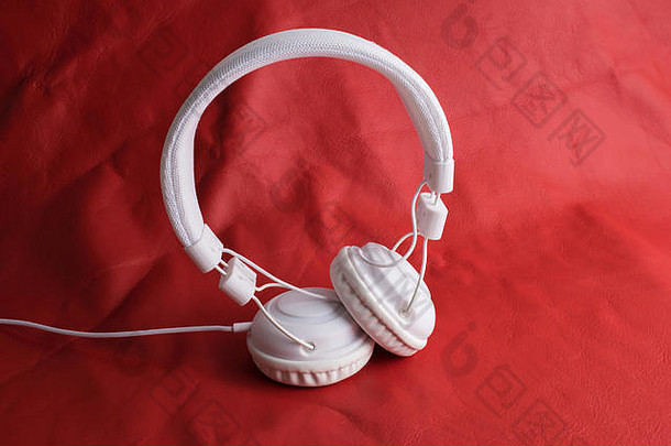红色皮革背景上的独立现代白色耳机。