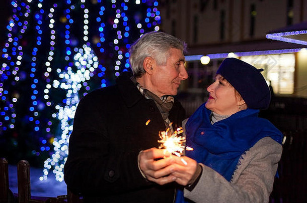 一对年长的家庭夫妇在夜晚通过节日照明点燃火花。圣诞节和新年概念