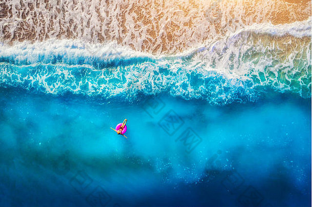 奥卢德尼兹透明海面上，一名女子在粉红色游泳圈上游泳的鸟瞰图。夏日的海景，女孩，海滩，美丽的海浪，蓝色的海水