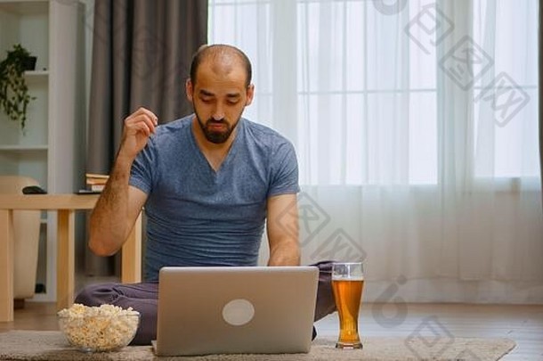 在冠状病毒封锁期间，愤怒男子喝啤酒的视频通话放大照片。