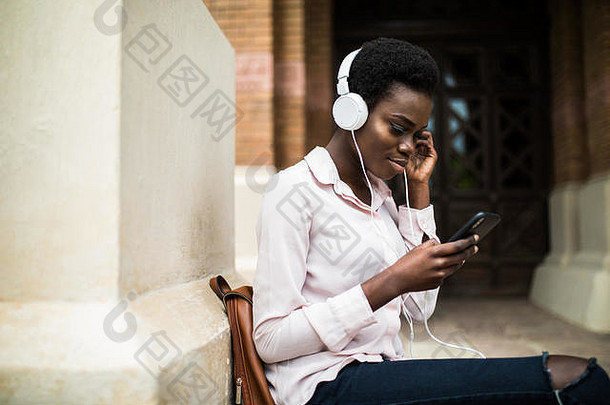 坐在长椅上，戴着耳机听音乐的美国黑人女孩。