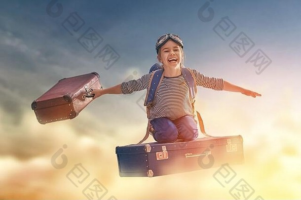 梦想旅行！在日落的背景下，一个孩子坐在手提箱上飞行。