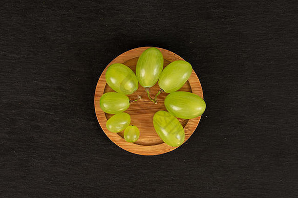 许多新鲜的绿色葡萄放在圆形的竹制杯垫上，平躺在灰色的石头上