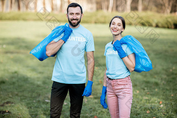 肖像快乐志愿者蓝色的t恤站袋完整的垃圾公园清洁