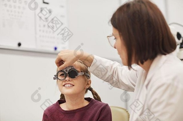 在现代眼科诊所<strong>检查</strong>小女孩视力时，女验光师设置试镜架的肖像，复印空间