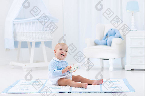可爱的婴儿男孩玩蓝色的地板上席喝牛奶瓶白色阳光明媚的托儿所摇摆椅子摇篮卧室以上室内