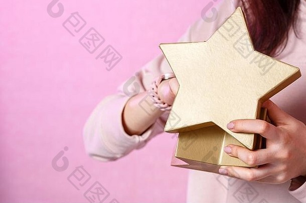 一个年轻的亚洲女孩手中的金星形状的礼品盒。在一个粉红色的孤立背景上