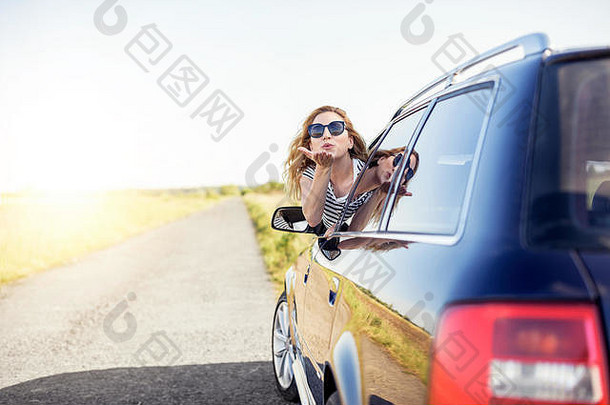 一个迷人的微笑的女人在夏天从车窗发出一个飞吻。