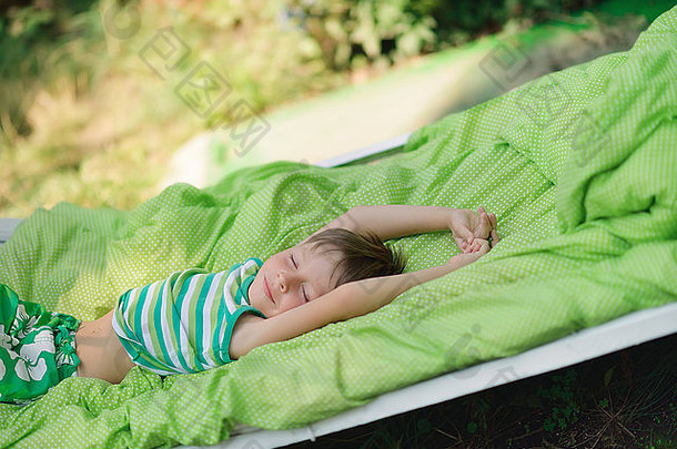 绿色的户外有一张白色的床，床上有一个可爱的小男孩