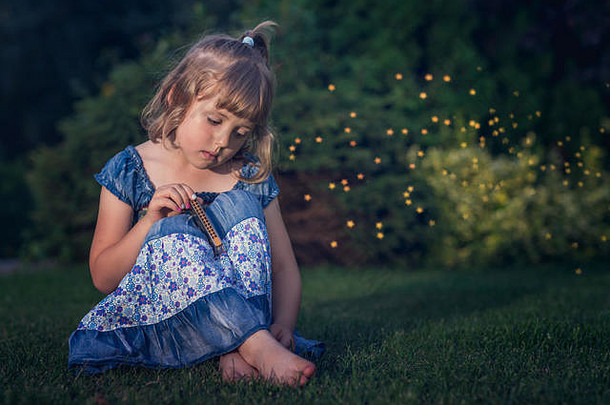 悲伤的赤脚女孩穿着蓝色的衣服坐在草地上，手里拿着她的小口琴