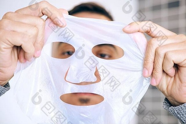一名白人男子即将在自己脸上贴上生物纤维素面膜的特写镜头