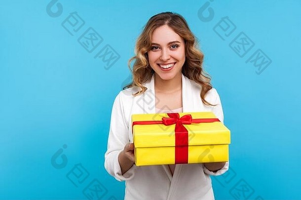 节日季节，一位快乐、心满意足的女人的肖像，一头卷发，穿着白色夹克，手里拿着黄色礼品盒，面带微笑看着相机。