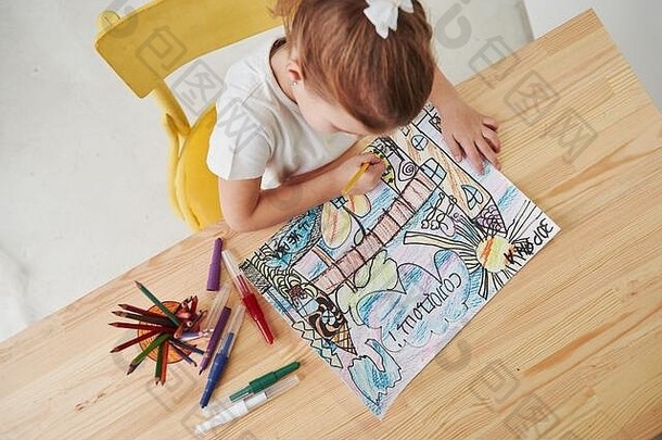 坐在黄色的椅子上。艺术学校里可爱的小女孩用铅笔和马克笔画出了她的第一幅画