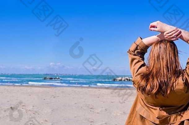 <strong>海边</strong>的女孩。棕色头发的女士望着远处的地平线。蓝天、沙滩和<strong>波涛</strong>拍岸。浪漫的照片。文本的可用空间。空间、横幅、长格式