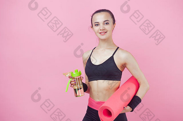 一位迷人的运动型浅肤色女孩的肖像，可爱，穿着紧身运动服，一只手拿着粉色<strong>瑜伽</strong>垫和一个运动用瓶子。