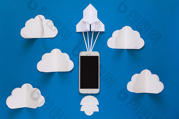 启动或快速连接概念。带智能手机的纸火箭在蓝天白云中发射。折纸。剪纸。俯视图