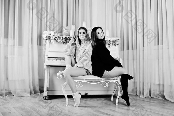 两个漂亮的女孩朋友穿着暖和的毛衣和暖腿套（绑腿）对抗圣诞蜡烛装饰的新年钢琴。