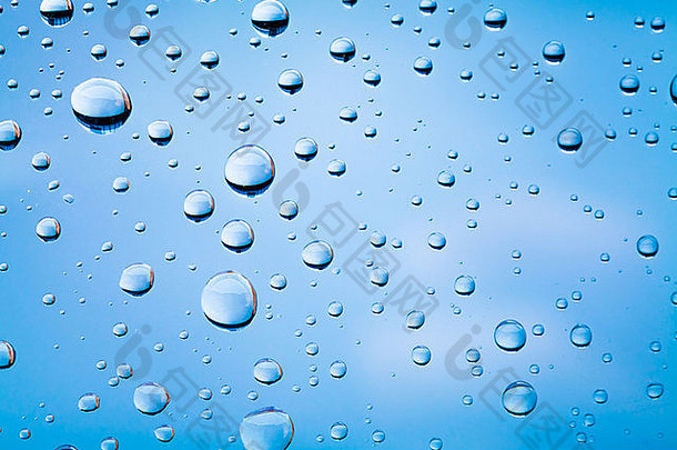 蓝色模糊天空上方玻璃上水滴的微距照片