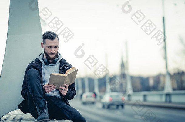 复古的风格照片年轻的赶时髦的人男人。坐着桥阅读书