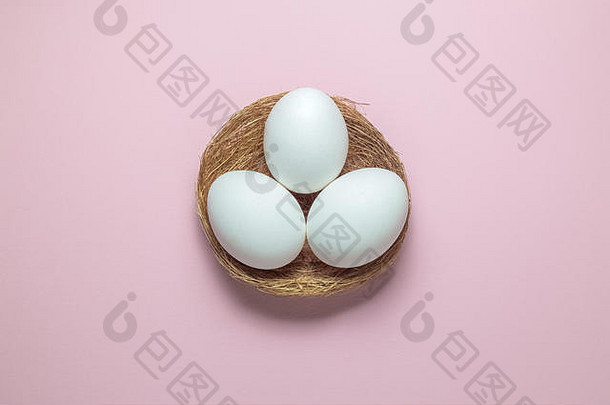 在纯粉色粉彩背景上鸟巢中白色卵的高角度视图。最小复活节概念