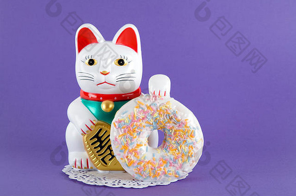一个maneki neko在一张纸上展示多色甜甜圈，背景是流行的彩色背景。极简古怪的彩色静物摄影