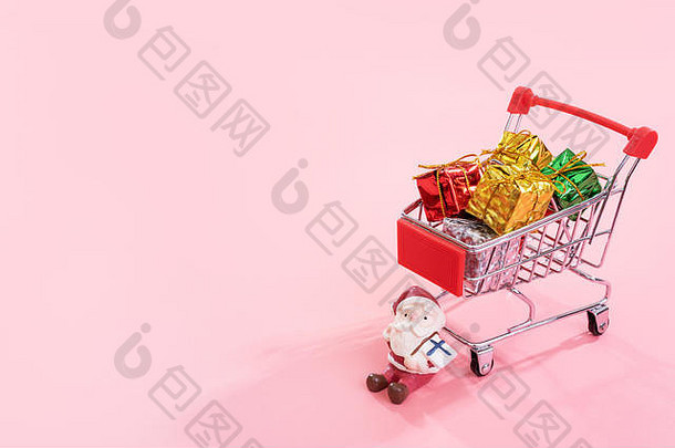 圣诞购物概念，迷你红色购物车手推车，带圣诞老人玩具和礼品盒，背景为淡粉色，空白空间，特写