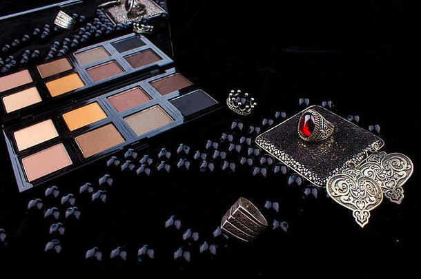 化妆工具和银配件在毛皮黑色背景/特色眼影调色板，银戒指和耳环在一个愤怒的黑色背景
