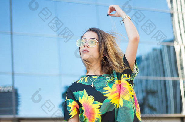 年轻的女人色彩斑斓的花衬衫太阳镜摆姿势街
