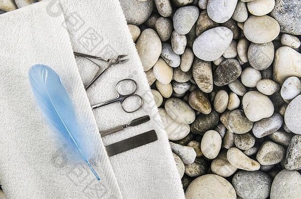 一套用于修甲和修脚的化妆工具。指甲剪、角质层、白色毛巾上的锯子和蓝色钢笔放在海石背景上