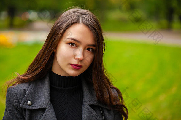 秋天公园里一位身穿灰色外套的年轻漂亮黑发女子的肖像