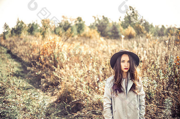 户外时尚照片，年轻美丽的女士在秋天的风景与干花。灰色的外套，黑色的帽子，葡萄酒口红。温暖的秋天。暖春