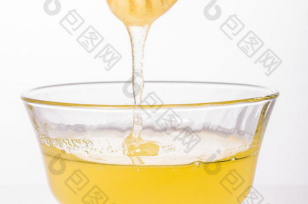 新鲜蜂蜜从木勺上滴下，隔离在白色表面