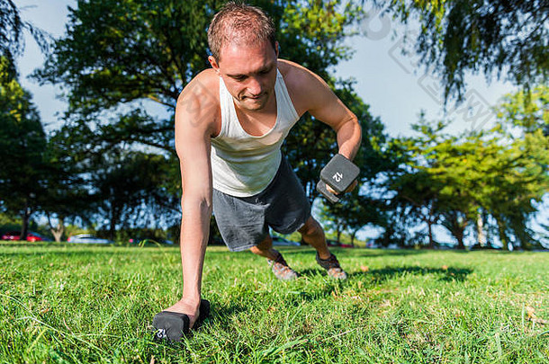 年轻健康男子在草地上举起哑铃的特写镜头