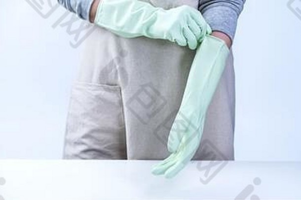 穿着围裙的年轻女管家戴着绿色手套清洁桌子，白色背景上的防病毒感染概念，特写镜头。